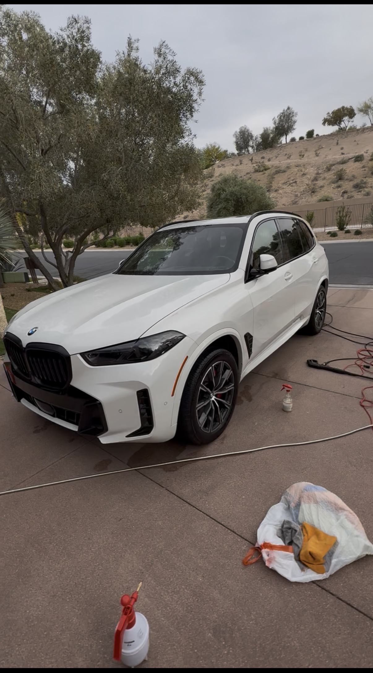 White BMW X5 detailed in a driveway with cleaning supplies nearby